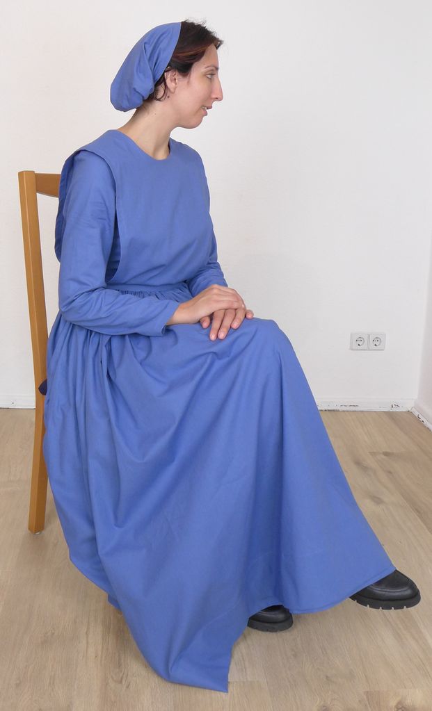 Side view of a woman in a plain cape dress, sitting on a chair