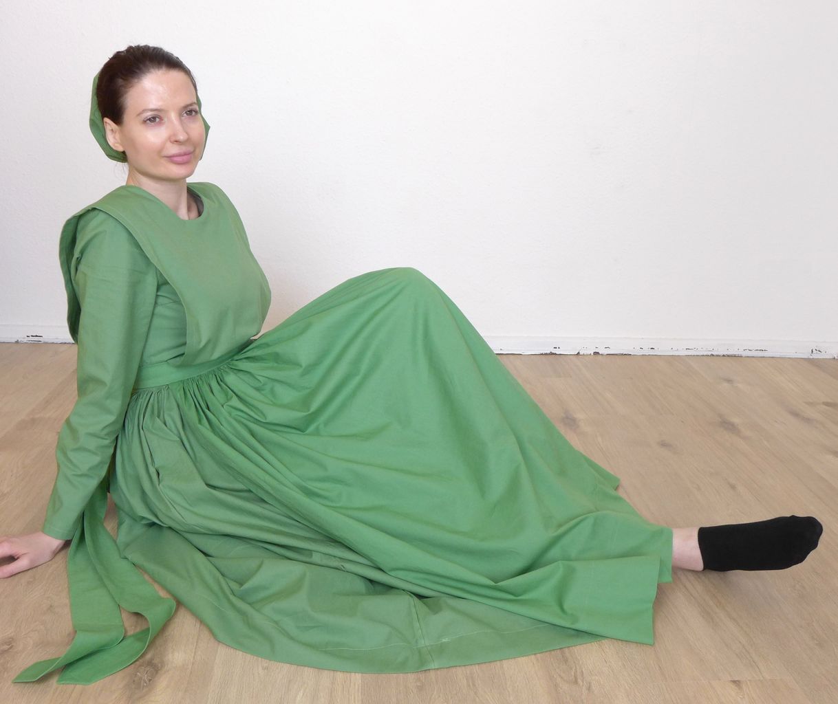 Side view of a woman in a plain cape dress sitting on the floor